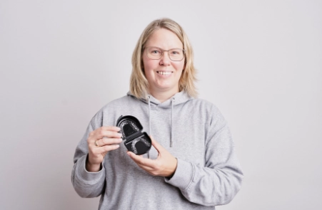 Eine glückliche Patientin von der ganzheitlichen Praxis für Kieferorthopädie Wolfratshausen hält Ihre Aligner Wolfratshausen in der Hand.